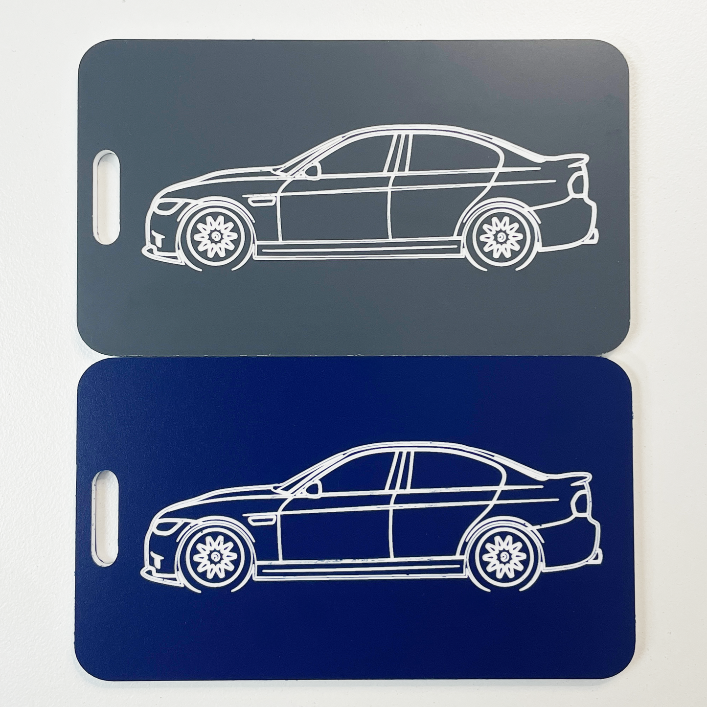 Two car-shaped luggage tags, one gray and one blue, on a light gray background.