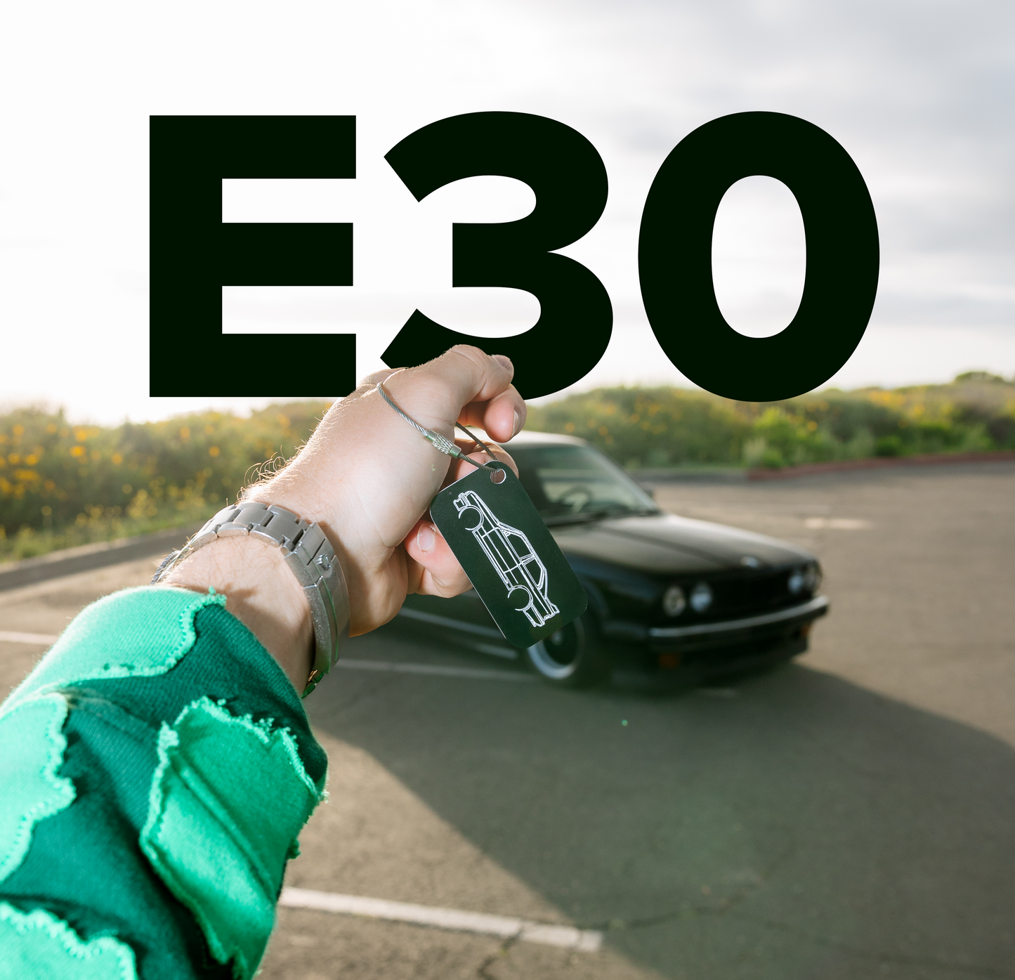 Picture of a BMW E30 M3 Acrylic Keychain in black with an e30 m3 behind.