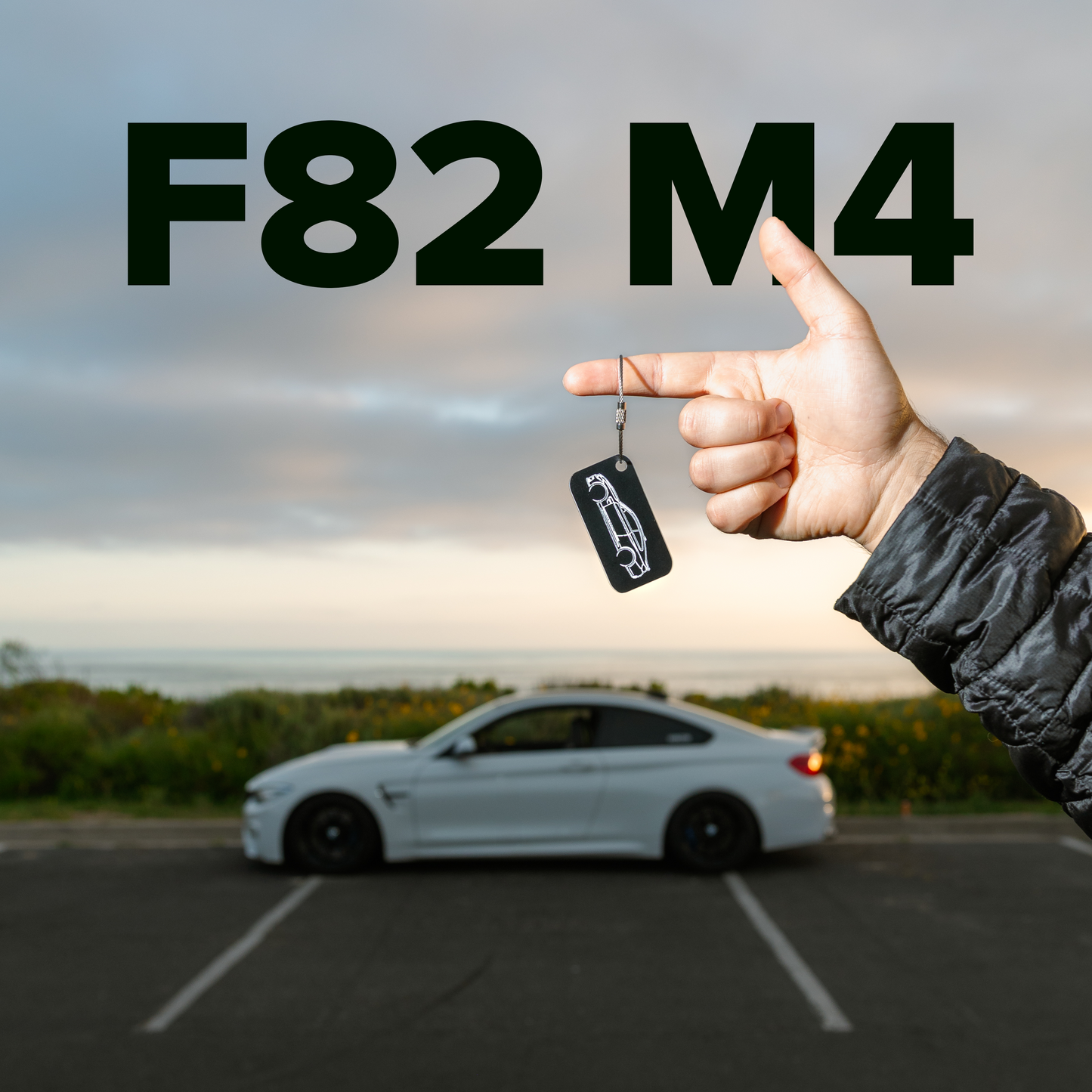 Picture of F82 M4 Acrylic Keychain in black hanging from person's hand with F82 M4 in background.