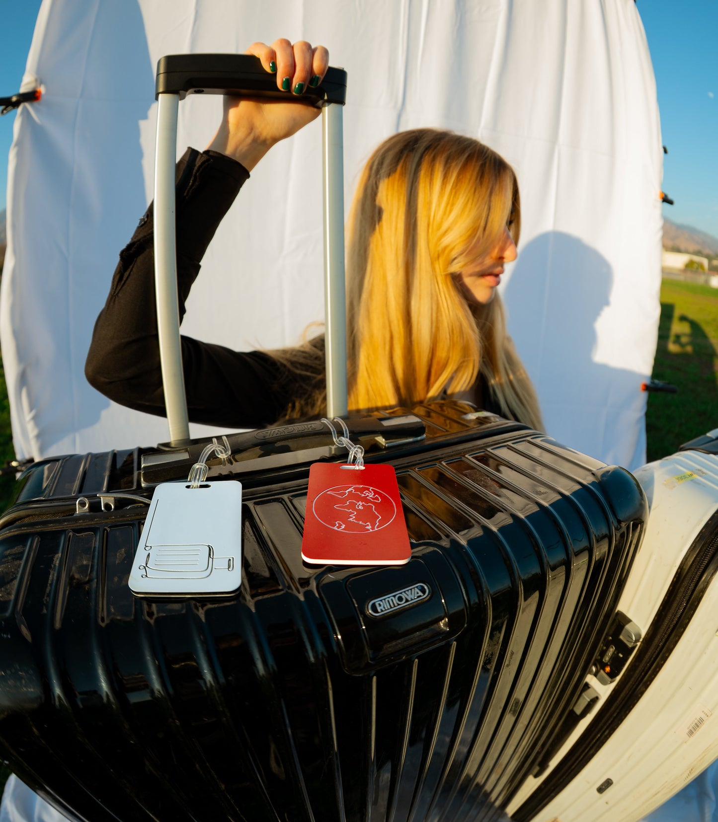 Explorer Design Luggage Tag in white attached to black Rimowa suitcase.