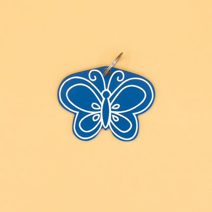 Blue butterfly-shaped keychain with classic key ring on a beige background
