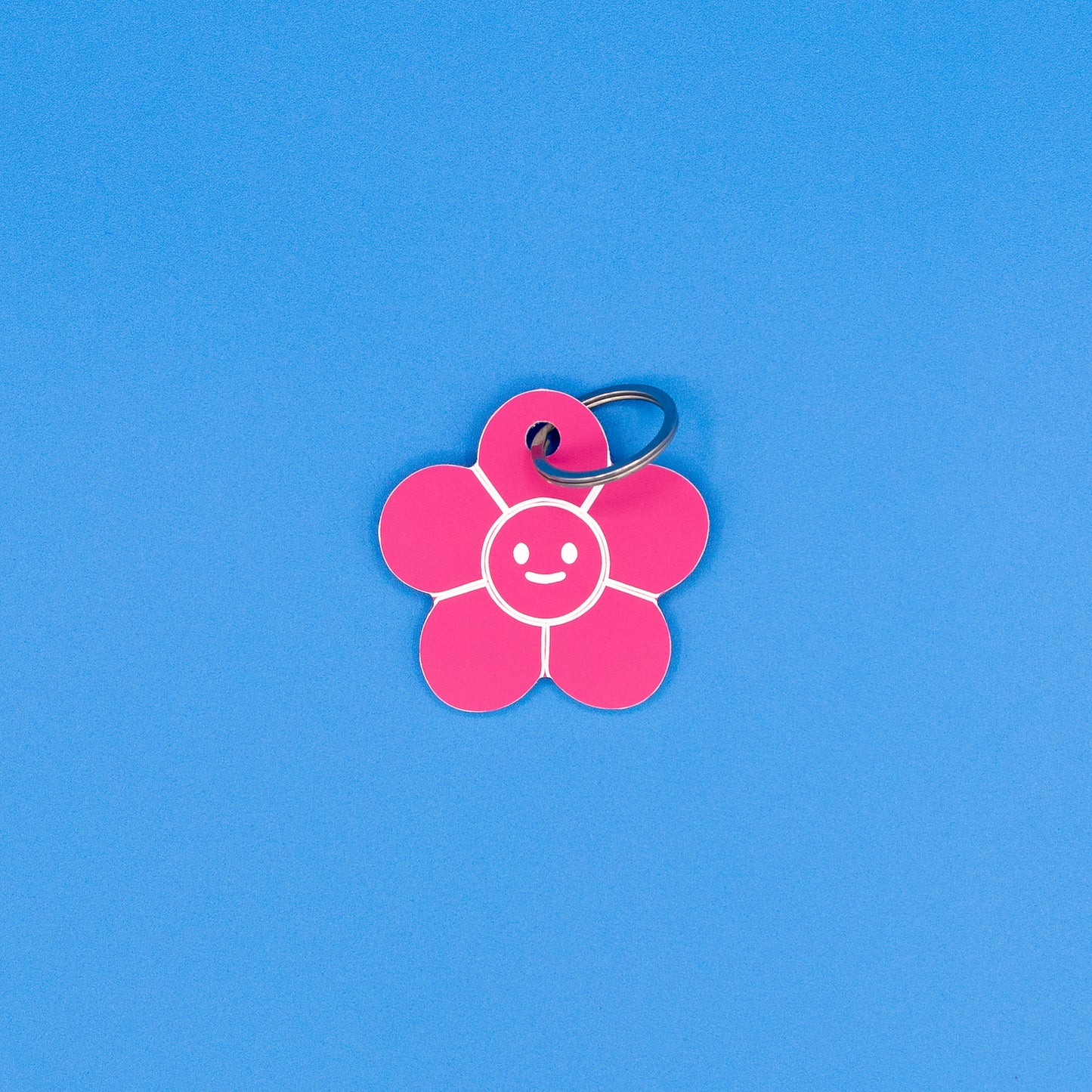 Pink flower-shaped keychain with a smiley face on a blue background