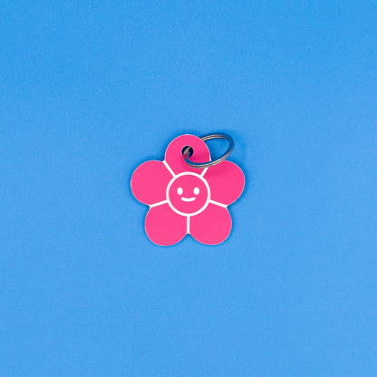 Pink flower-shaped keychain with a smiley face on a blue background