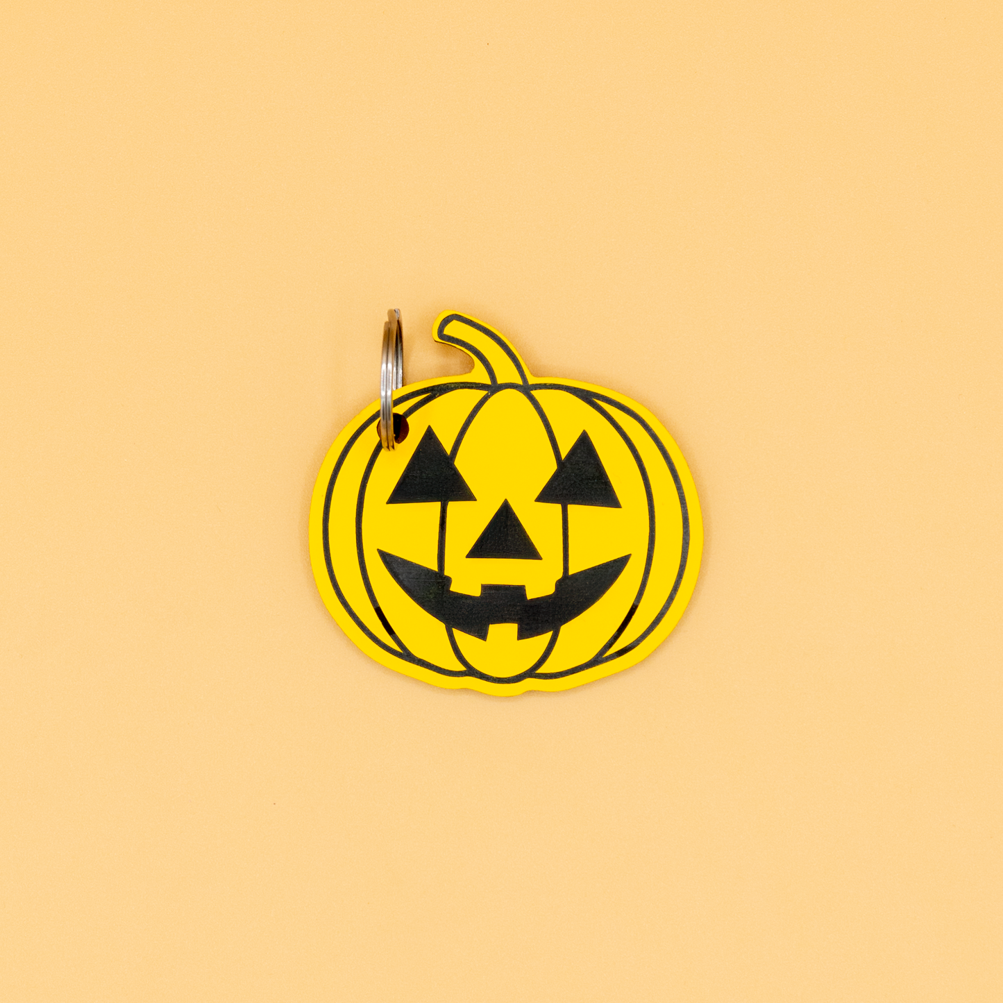 Pumpkin-shaped keychain with classic key ring with black face design on a beige background
