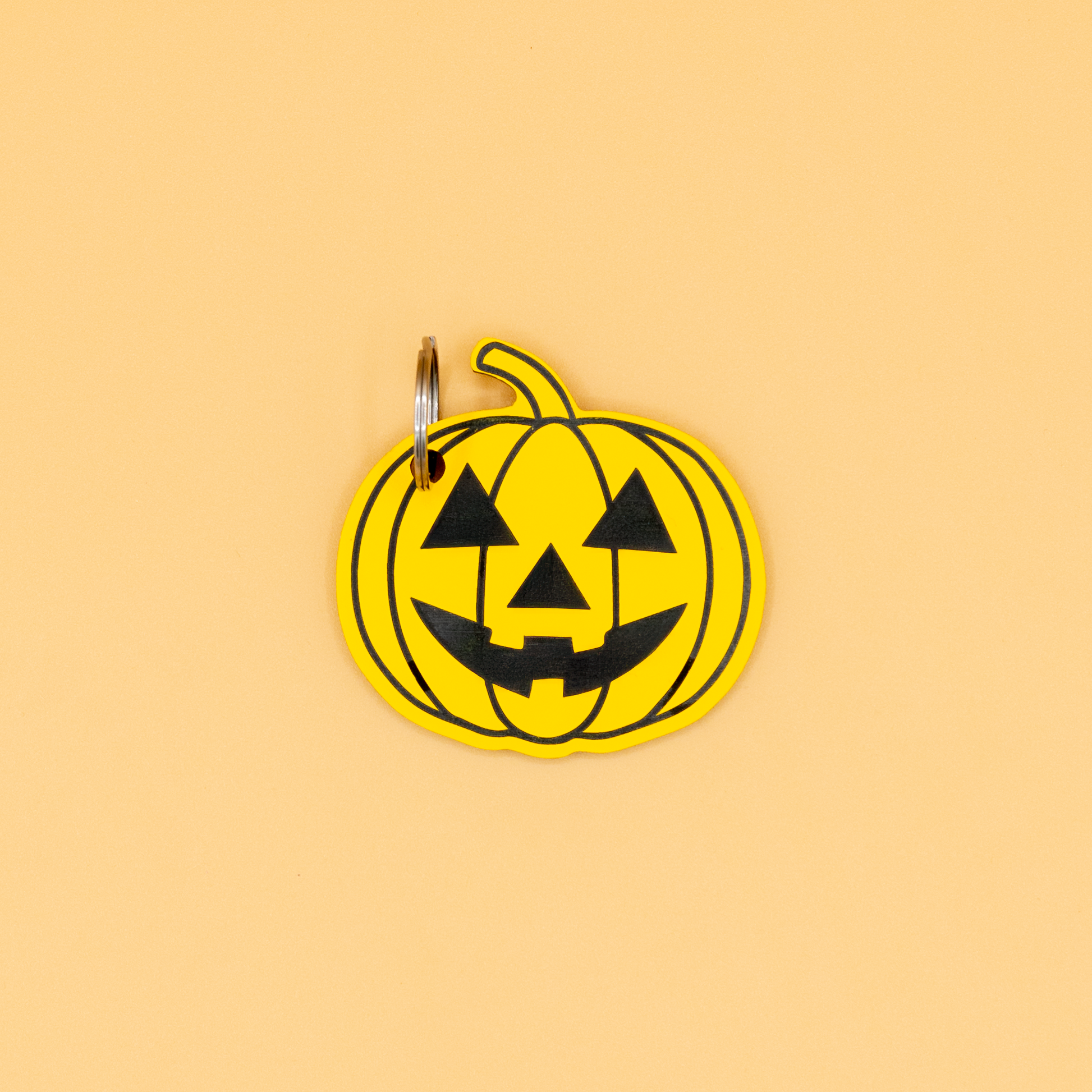 Pumpkin-shaped keychain with classic key ring with black face design on a beige background