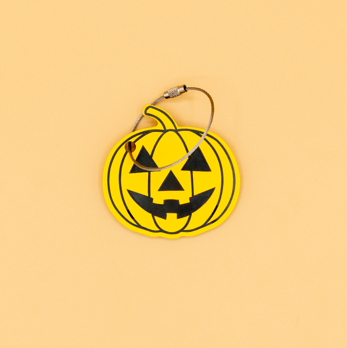 Yellow pumpkin-shaped keychain with wire loop with black details on a beige background