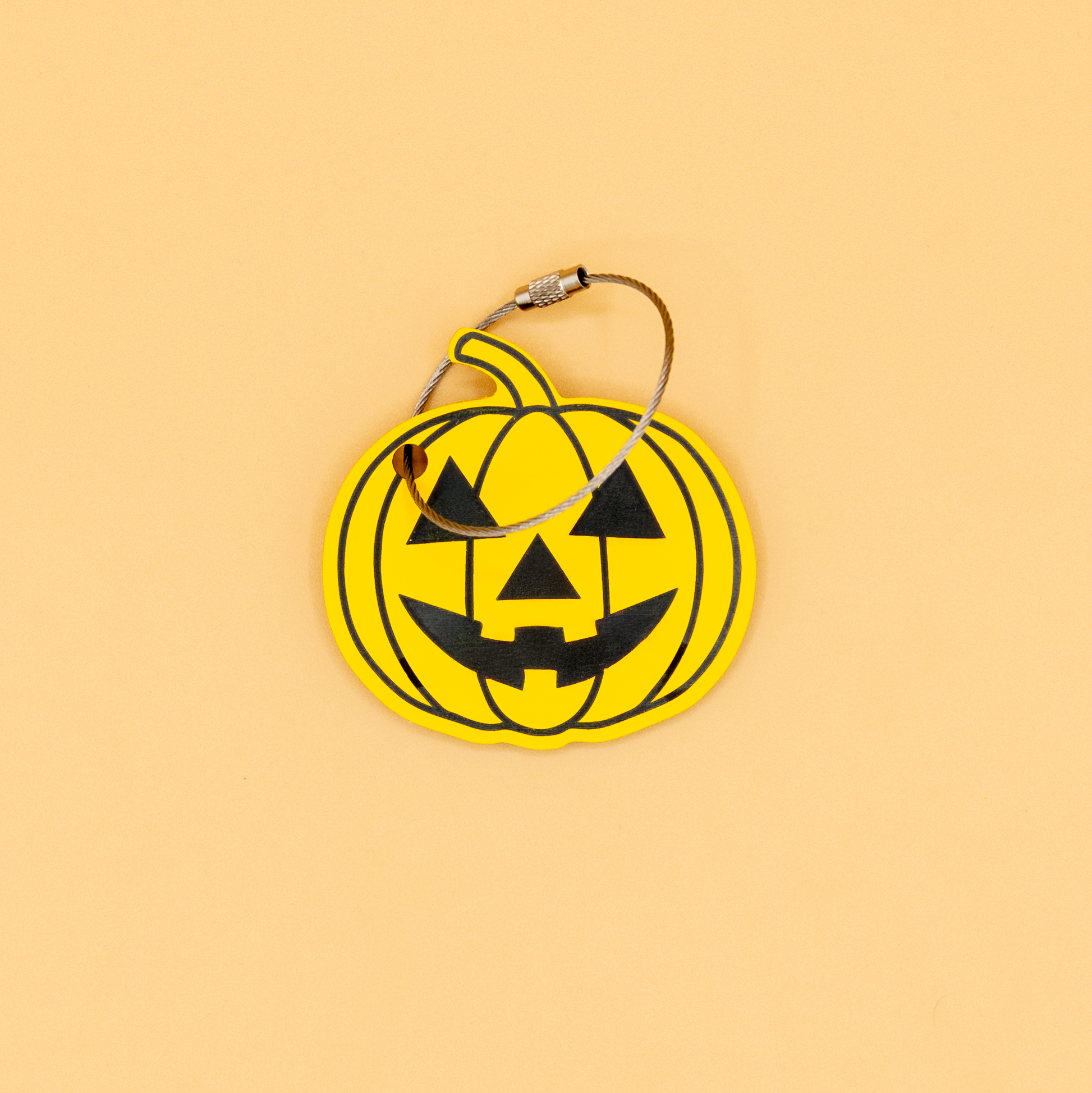 Yellow pumpkin-shaped keychain with wire loop with black details on a beige background