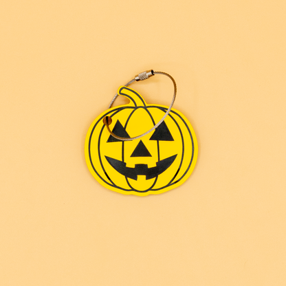 Yellow pumpkin-shaped keychain with wire loop with black details on a beige background