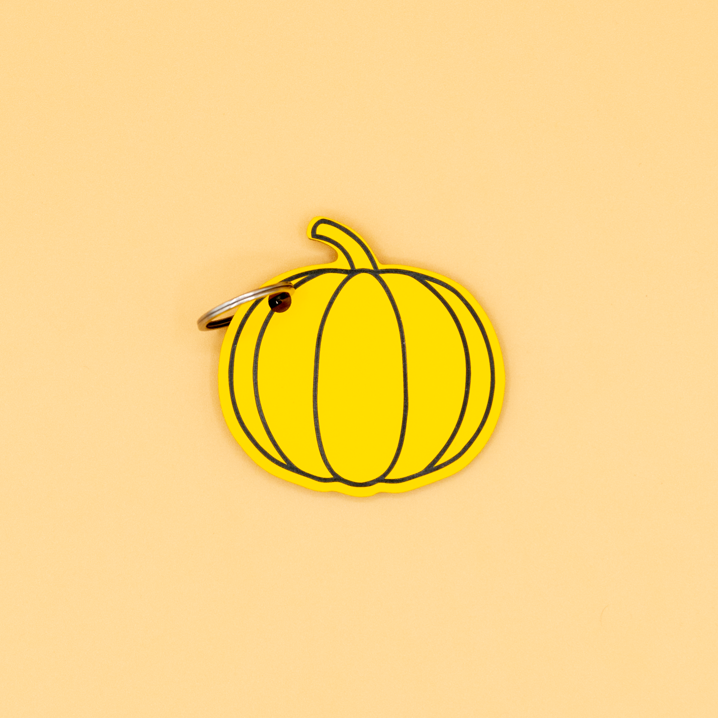 Yellow pumpkin-shaped keychain with classic key ring on a beige background