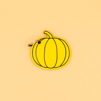 Yellow pumpkin-shaped keychain with classic key ring on a beige background