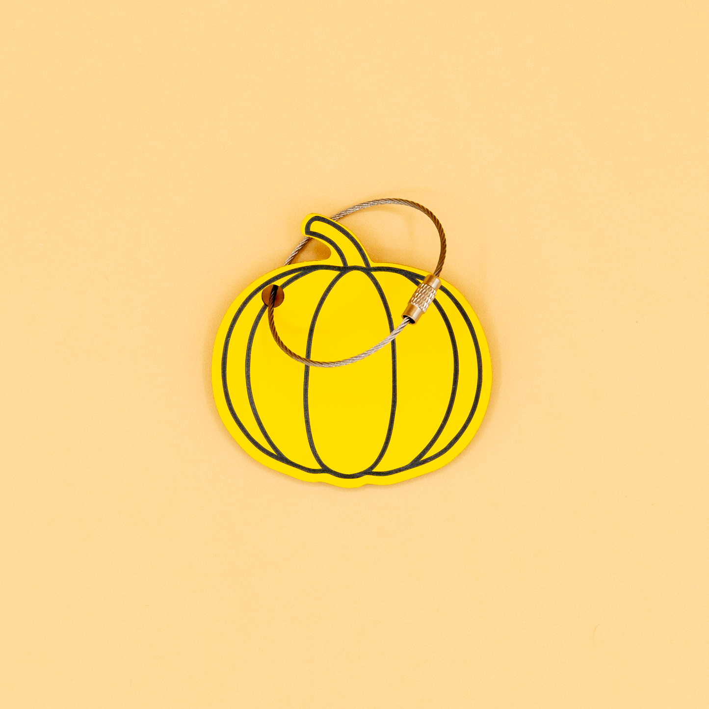 Yellow pumpkin-shaped keychain with wire loop on a beige background