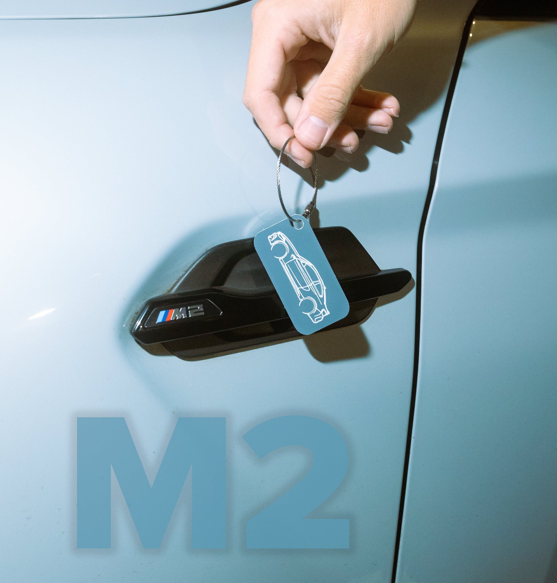 BMW F87 M2 Acrylic Keychain in grey in front of an M2 Badge.